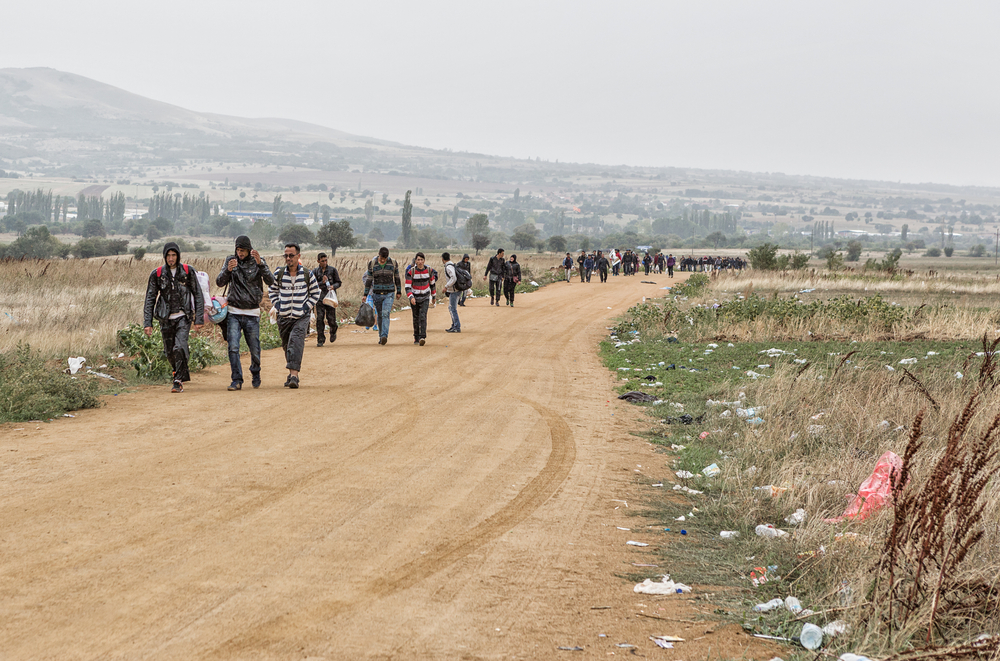 Refugees and migrants walking the dusty road in the rain to the