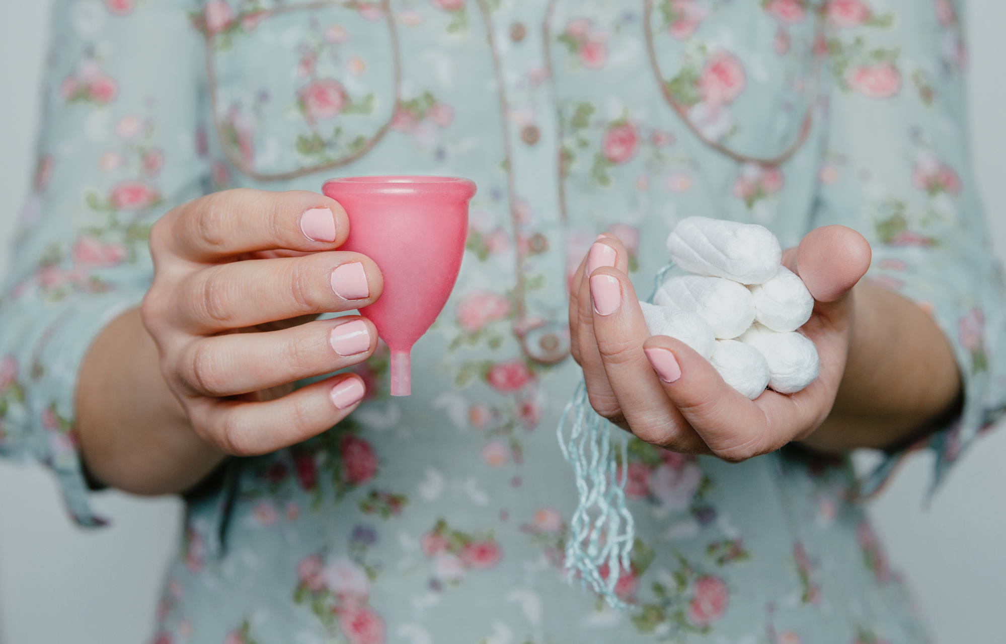Manos de mujer sosteniendo una copa menstrual y tampones